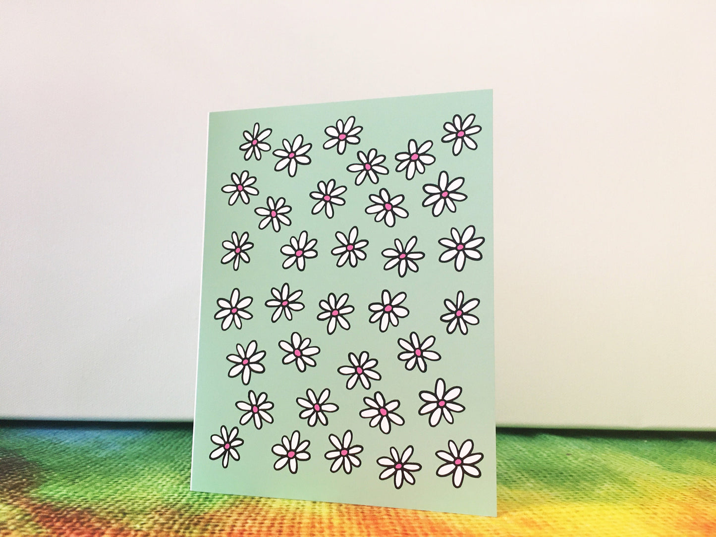 A greeting card standing opened on top of a table and the cover image features dozens of white daisies on a light green background.