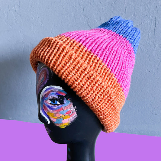 A black mannequin with a colorfully painted face wearing the orange-pink-blue color block beanie