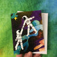 A hand holding a greeting card featuring an illustration of two astronauts floating in space while holding hands. The inside of the card reads, "you take me to outerspace."