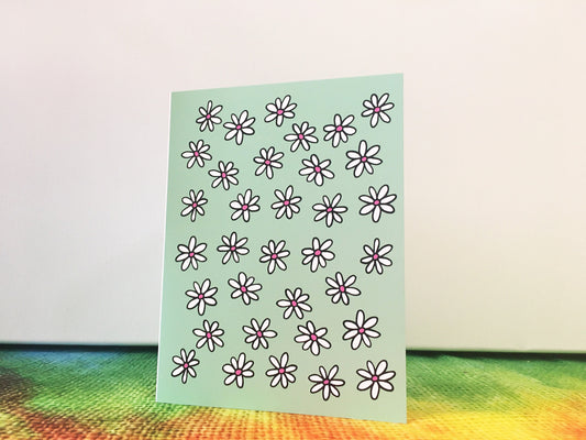 A greeting card standing opened on top of a table and the cover image features dozens of white daisies on a light green background.